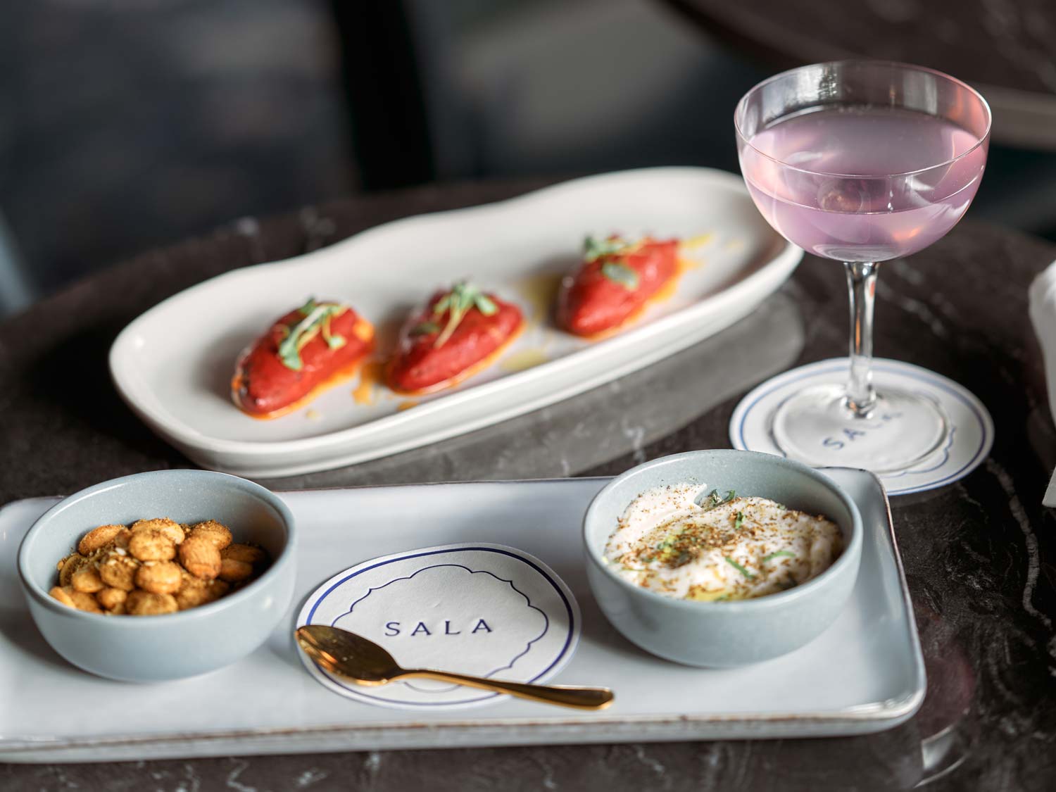 table with two plates of elegant appetizers and a purple cocktail